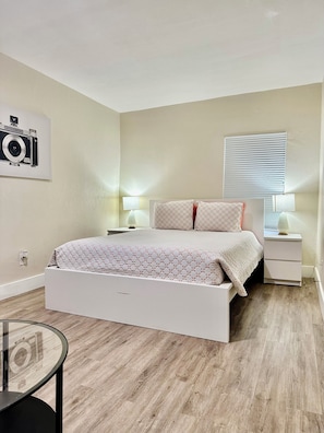A bedroom with a bed, bedside tables, a lamp, a camera on the wall, and a window with blinds. - Upstairs 2BR · Fire Pit Yard · Laundry · Fast WiFi · Monthly Deals · Near Beach (Daytona Beach)