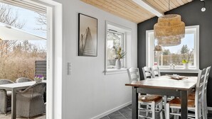 A dining area with a wooden table and white chairs, a hanging rattan light fixture, and a window with a view of trees. - Nice home in Græsted with WiFi (Græsted)
