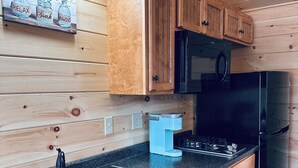 A kitchen with wooden cabinets, a black refrigerator, a coffee maker, and a sink. - Green Cabin in Surry close to Acadia and Bar Harbor (Surry)