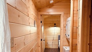 A narrow wooden hallway with a ceiling light, wooden walls, and a small white appliance on the right. - Green Cabin in Surry close to Acadia and Bar Harbor (Surry)