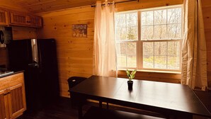 A wooden cabin interior with a kitchen area, a dining table with benches, and a window with curtains. - Green Cabin in Surry close to Acadia and Bar Harbor (Surry)