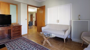 Ein Wohnzimmer mit einer Couch, einem Glastisch, einem Fernseher, Holzmöbeln und einem gemusterten Teppich.