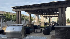 Un patio al aire libre con una parrilla, asientos y una estructura de pérgola.