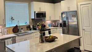 Una cocina moderna con armarios blancos, un refrigerador de acero inoxidable, un microondas y una isla grande con taburetes.
