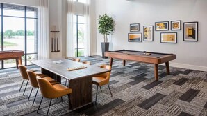 Una habitación moderna con una mesa de billar, una mesa de comedor con sillas y un amplio ventanal con cortinas.