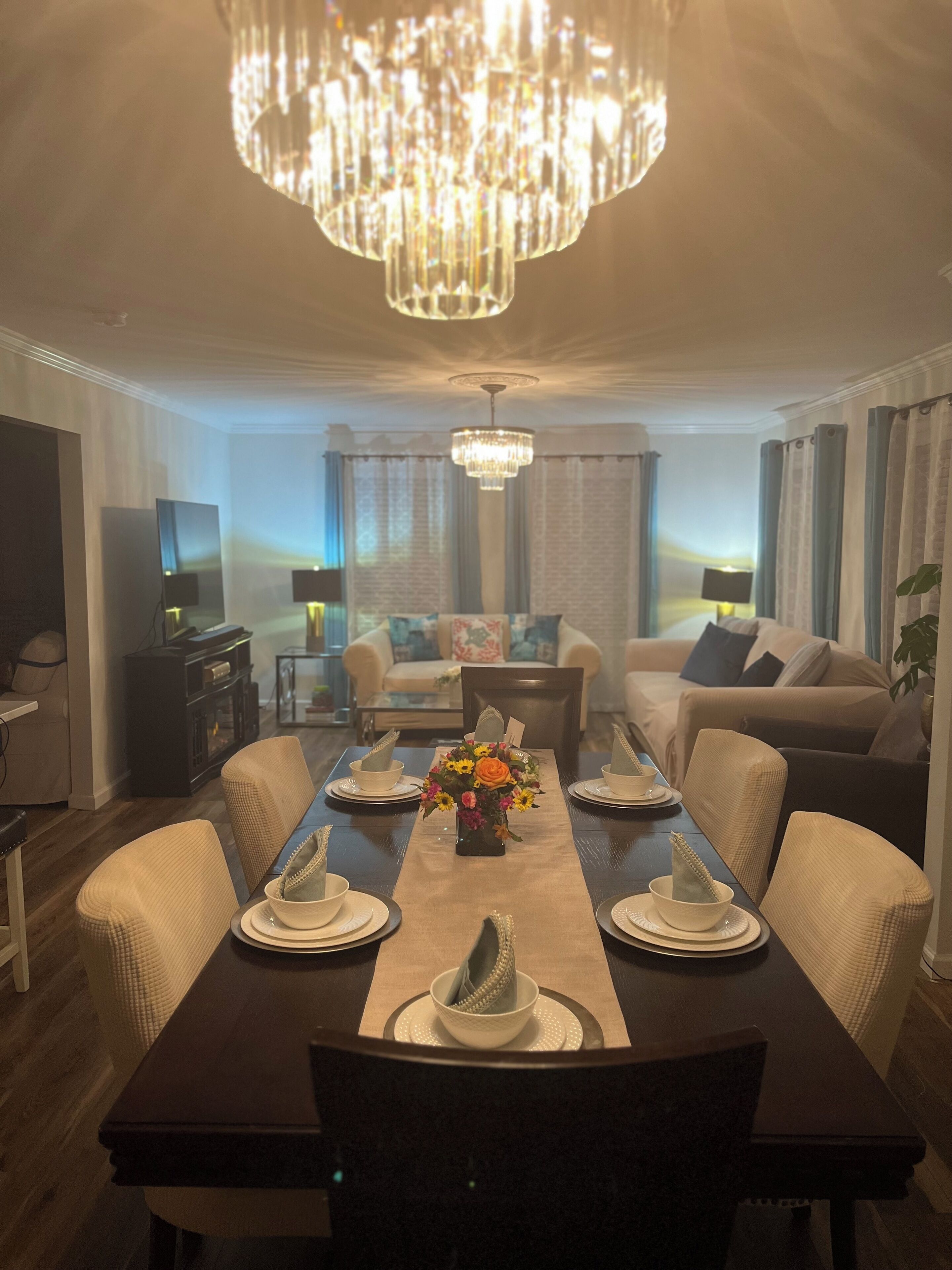 Un coin repas agrémenté d’un lustre, d’une table dressée pour quatre personnes et d’un canapé en arrière-plan.
