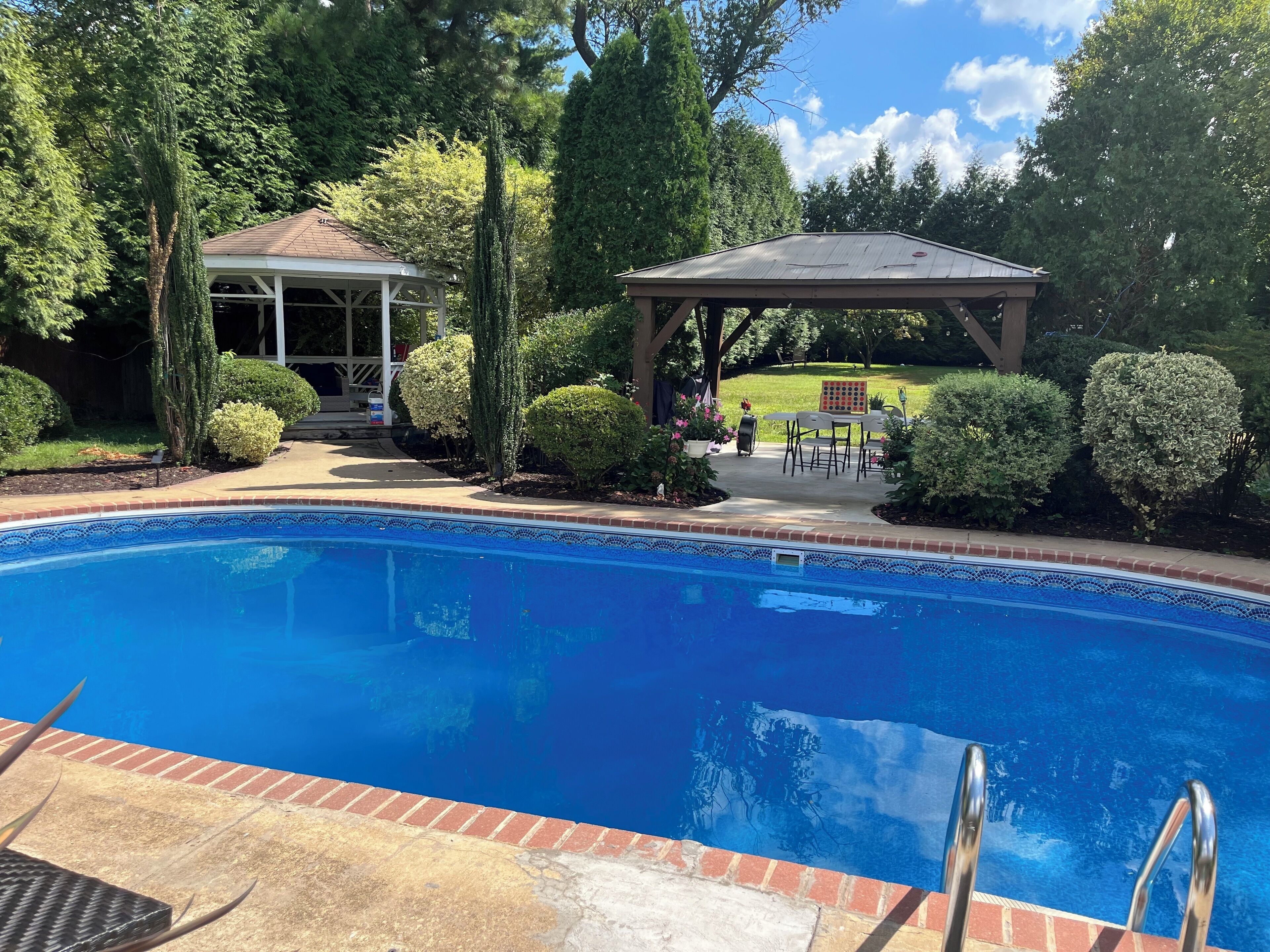 Une piscine dotée d’une terrasse carrelée, entourée d’arbustes et d’arbres bien entretenus.