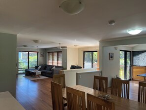 Uma sala de estar ampla, com mesa de jantar, cadeiras de madeira, sofá e ventilador de teto.