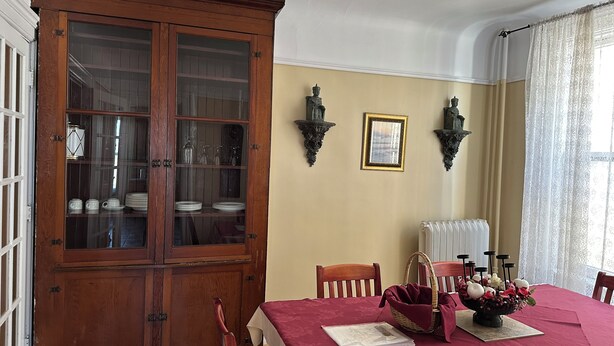 Un comedor con un aparador de madera, una mesa con mantel rojo y dos apliques de pared.