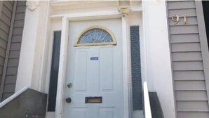 Una puerta blanca con el número 91 arriba, una pequeña ventana con una reja decorativa, y un buzón debajo.