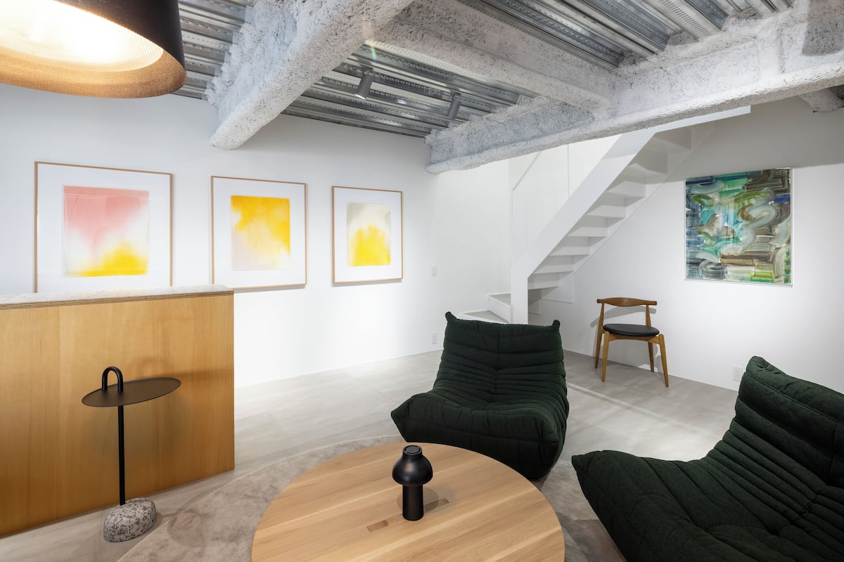 Un intérieur moderne avec un comptoir d’accueil en bois, des chaises recouvertes de tissu vert, une table ronde en bois et des œuvres d’art abstraites accrochées aux murs.