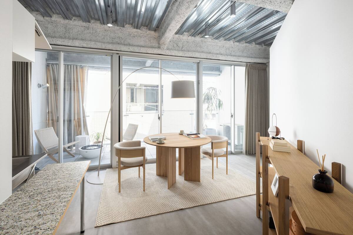 Un espace repas moderne avec une table ronde en bois, deux chaises, une grande fenêtre et une vue sur l’extérieur.
