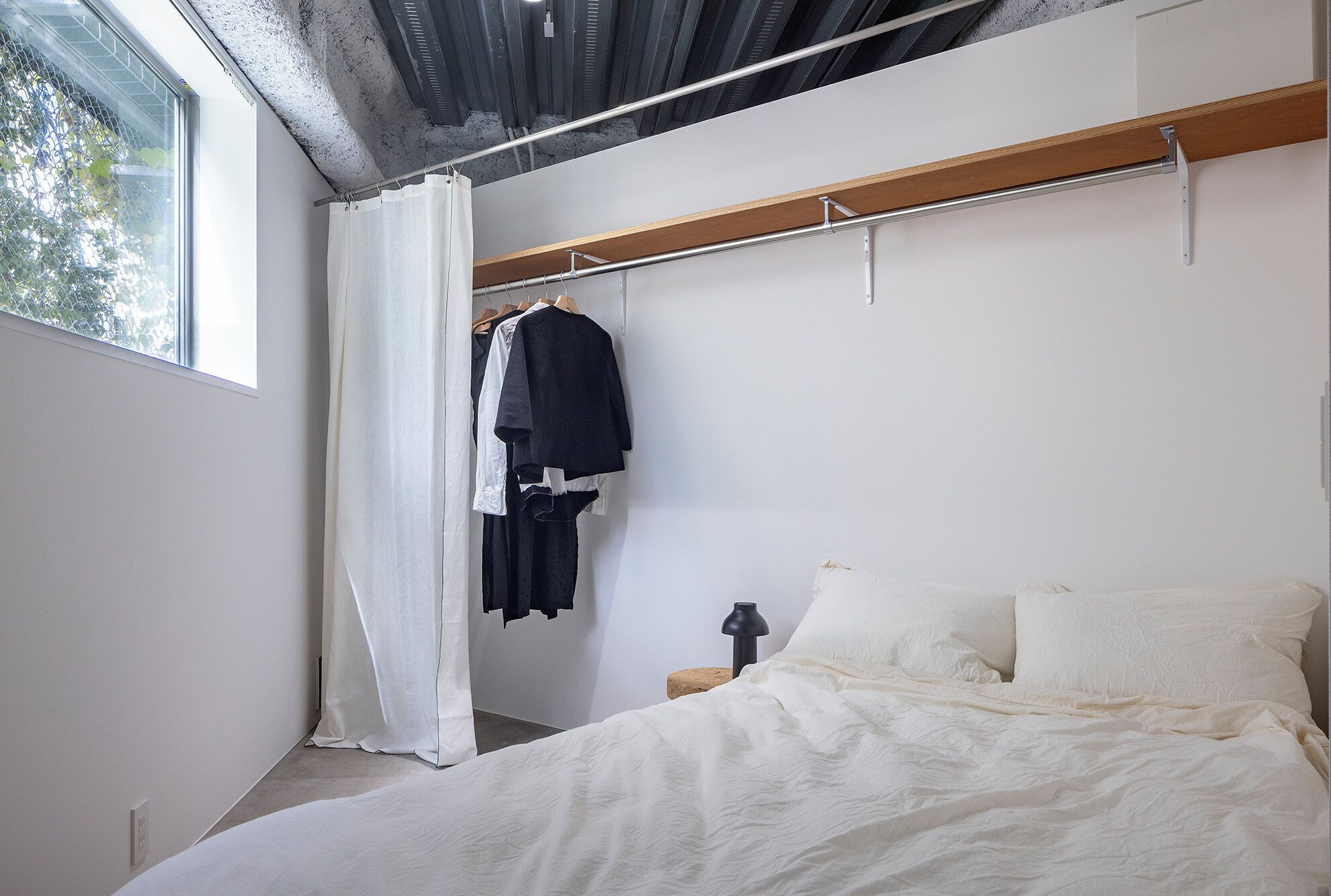 Un dormitorio con cama, cabecera de madera, perchero y ventana con cortinas.