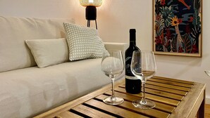 Una stanza con un tavolino in legno, un divano, una lampada decorativa, una bottiglia di vino e un'opera d'arte incorniciata.