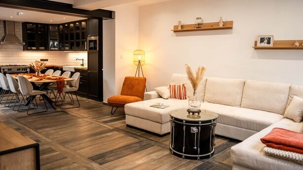 Uma sala de estar moderna com área de jantar, um sofá, um banquinho cilíndrico e uma luminária.