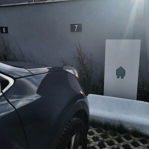 Un coche negro estacionado junto a un edificio con el número 7 y una puerta blanca con un símbolo de vivienda.