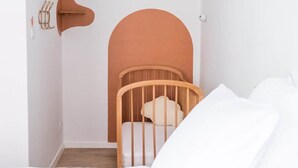 Quarto minimalista com berço de madeira, roupa de cama branca e parede branca lisa com uma luminária embutida no teto.