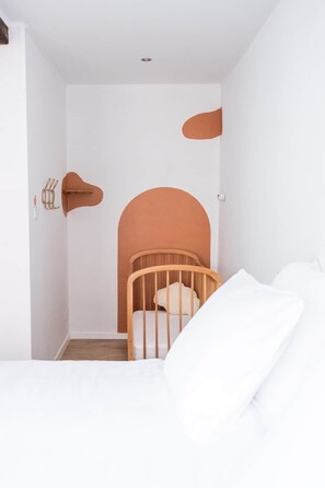 A minimalist room with a wooden crib, white bedding, and a plain white wall with a recessed ceiling light. - Gite à binche - A l'Orange Sanguine (BINCHE)