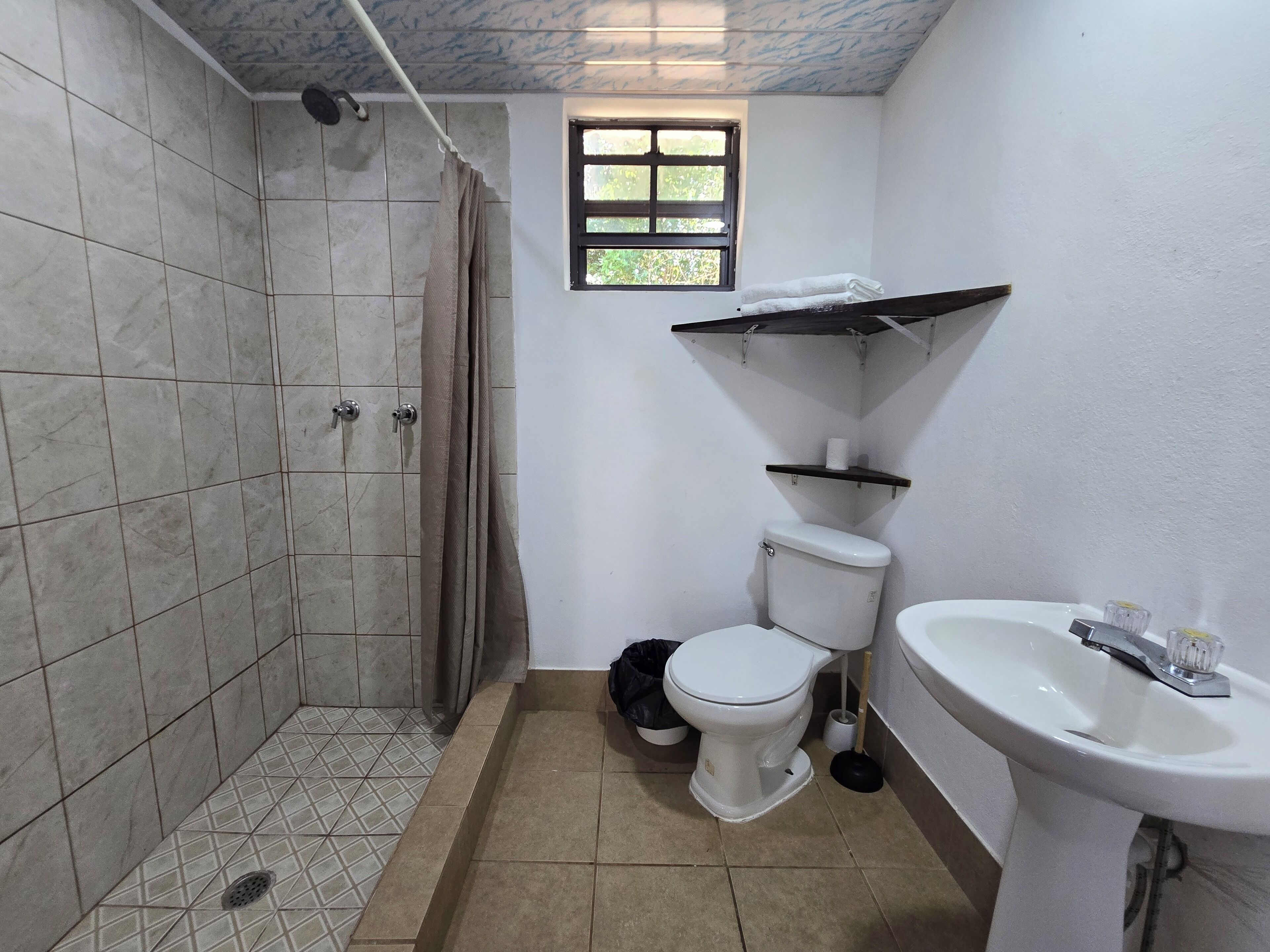 A bathroom with a shower, toilet, sink, and a window.