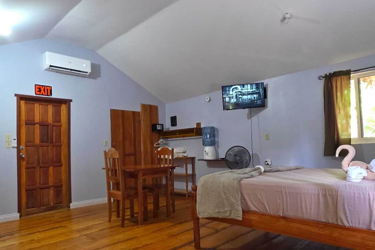A room with a bed, a desk, a chair, an air conditioner, a TV, and an exit sign.