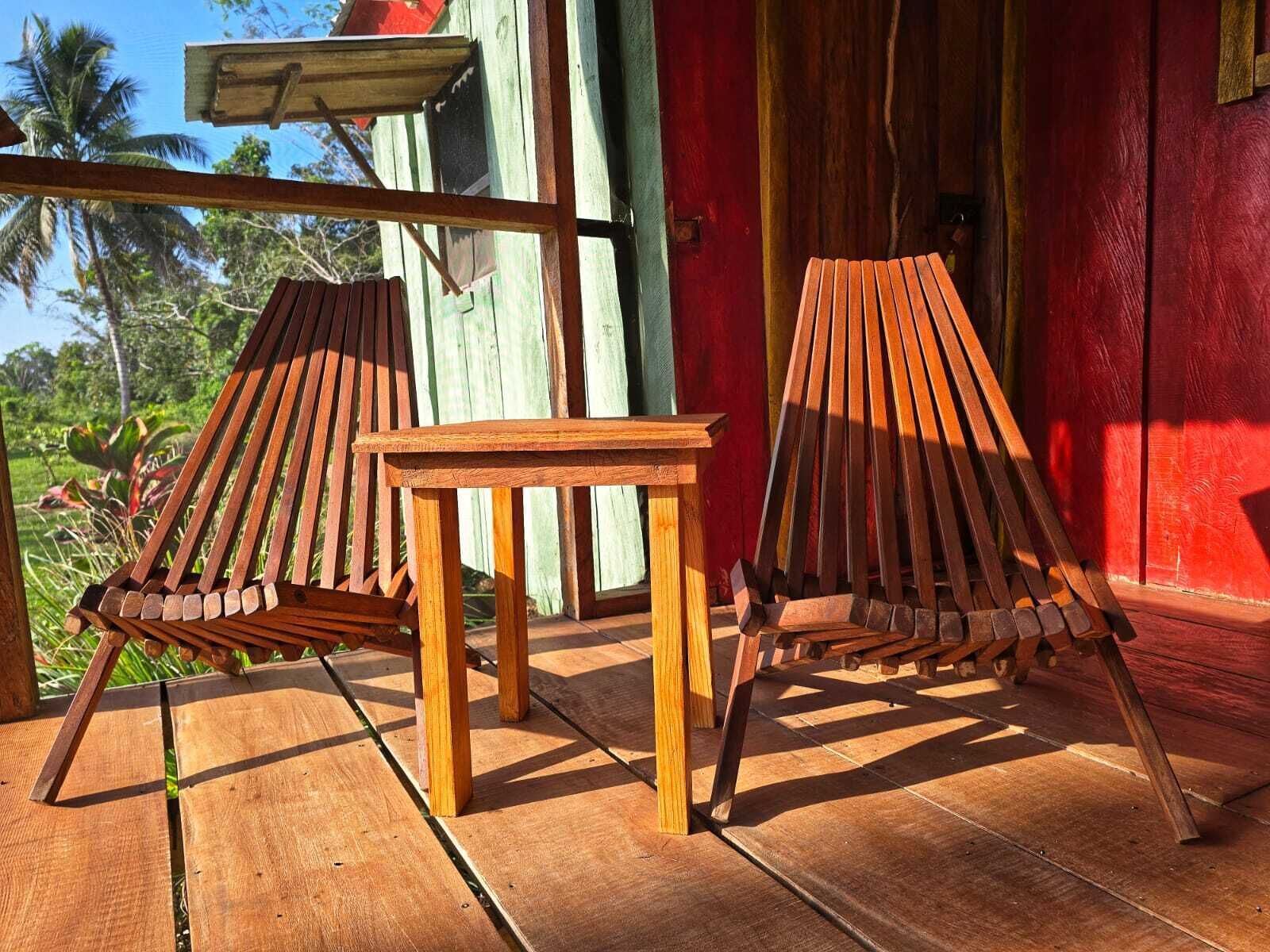 Two wooden lounge chairs and a small table on a wooden deck with a red wall in the background.