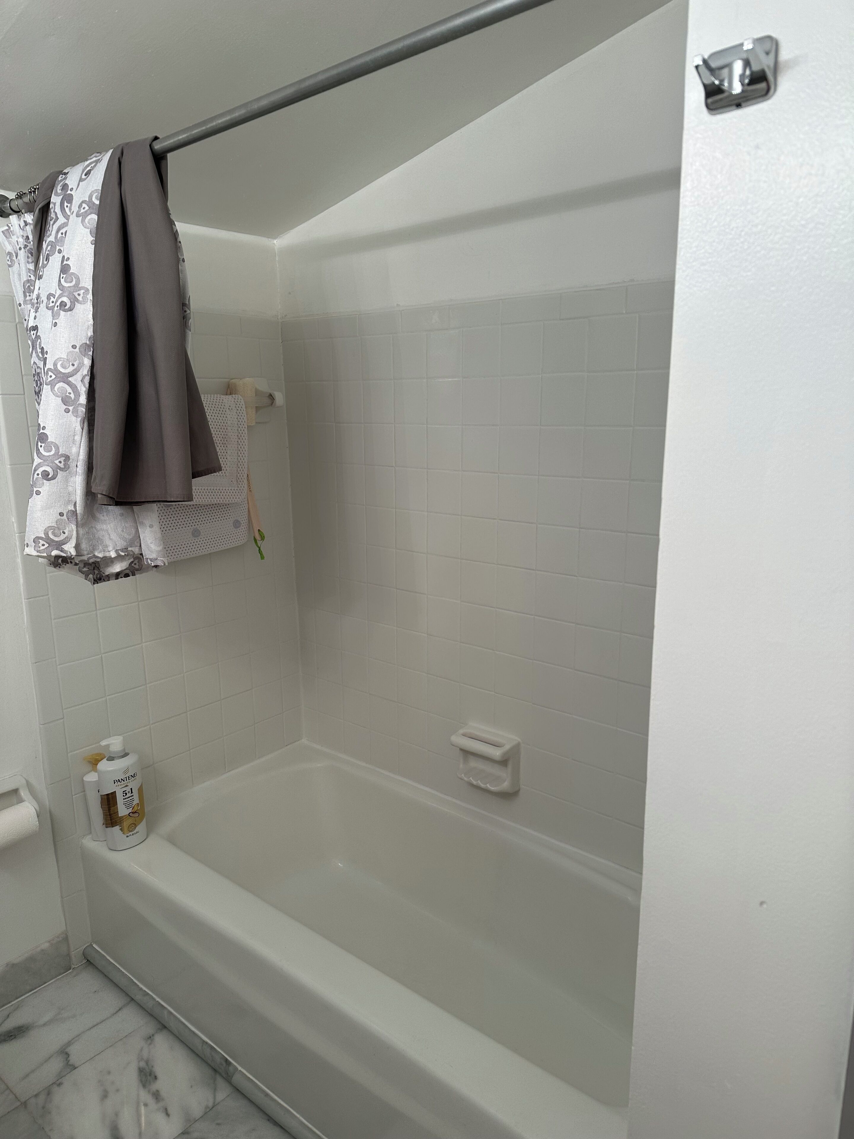A bathroom with a bathtub, a towel rack with a towel, a soap dispenser, and a bottle of Pantene shampoo.