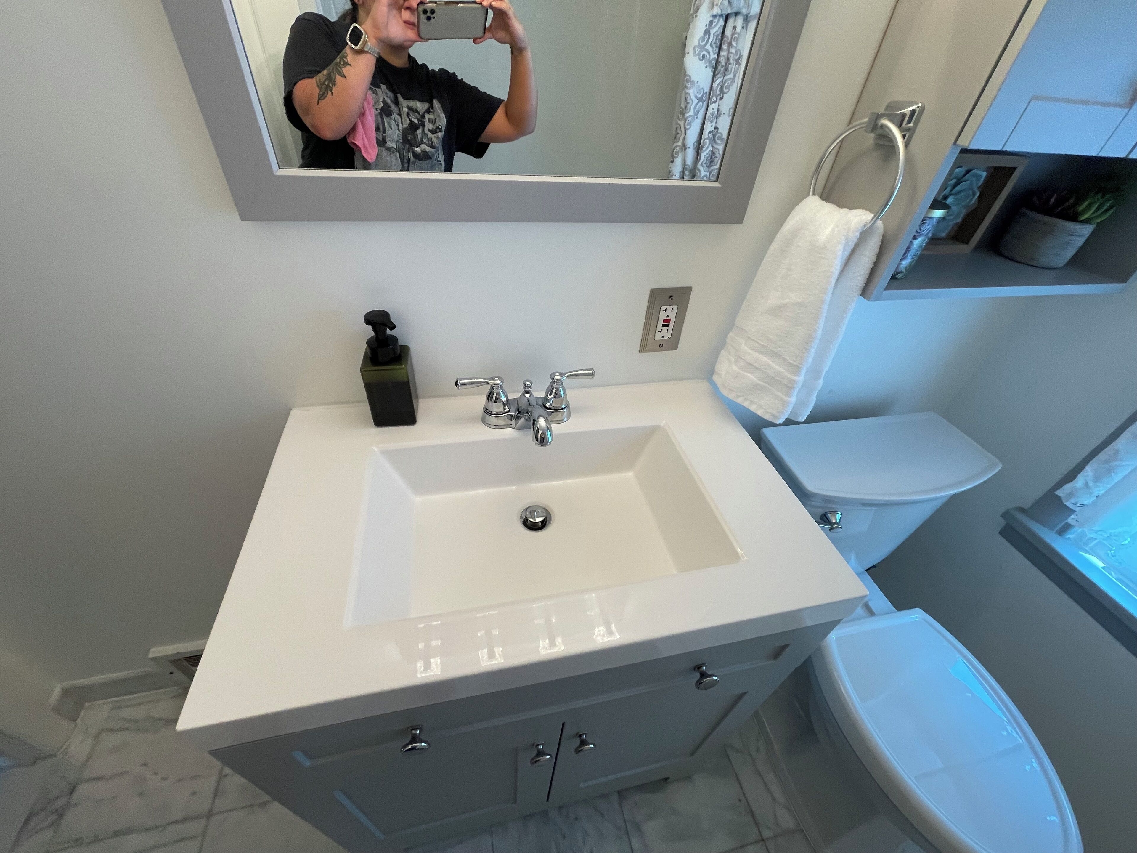 Un baño con lavamanos blanco, espejo, toallero y retrete.
