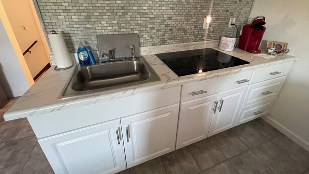A kitchen with a sink, a stovetop, and a microwave. There is a brick backsplash and a sign that says "being kind". - Charming 1-bedroom apartment with AC, WiFi in beautiful Fairport (Fairport)
