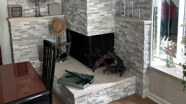 Una sala de estar con chimenea de piedra, una mesa de comedor y sillas. Hay objetos decorativos en la repisa y un espejo que refleja parte de la habitación.