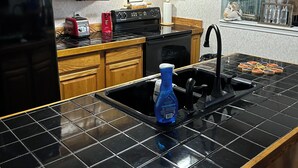 Una cocina con armarios de madera, encimera de baldosas negras, un lavamanos de acero inoxidable y ollas de cobre colgantes.
