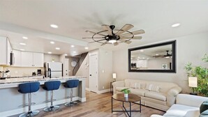 A modern kitchen with a central island, bar stools, a ceiling fan, and a living area with a sofa and a coffee table. - Cozy Boise Stay: Central Spot (Boise)