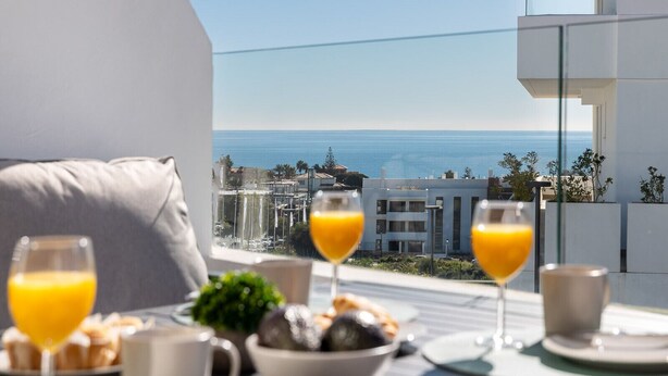 Un balcón con una mesa dispuesta para el desayuno, con vistas a la costa.