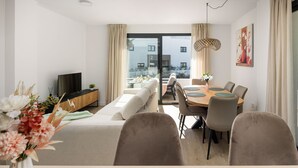 Una sala moderna con sofá, mesa de comedor, sillas, televisor y un amplio ventanal con vistas a edificios.
