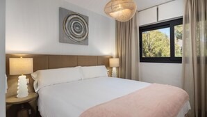 Un dormitorio con una cama grande, dos lámparas de noche, un cuadro en la pared y una ventana con cortinas.