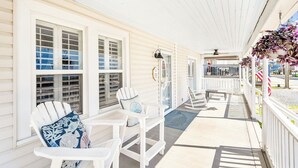 A covered porch with white railings, a seating area with white chairs and blue patterned cushions, and a small table. - CB Surf House|Charming Beach House 2mins to Beach (Carolina Beach)