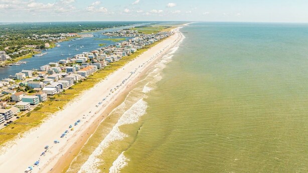 An aerial view of a coastal town with a long sandy beach, rows of buildings, and boats in the water. - CB Surf House|Charming Beach House 2mins to Beach (Carolina Beach)