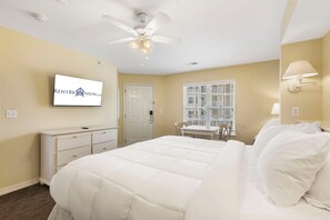 Una habitación de hotel con cama, escritorio, silla, televisor y ventilador de techo.