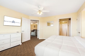 A bedroom with a bed, dresser, ceiling fan, and a door leading to another room.