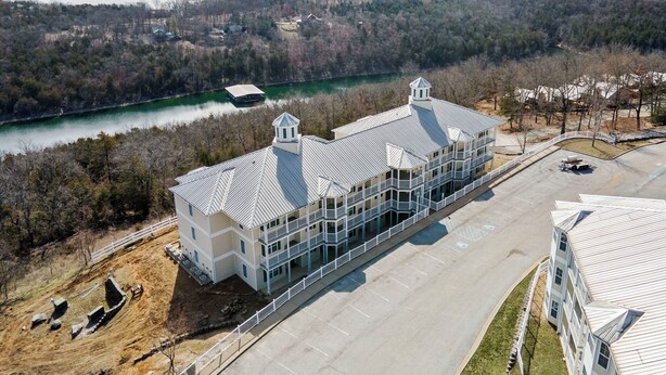 A large, multi-story building with a flat roof, located near a body of water and surrounded by trees. - Relaxed Lake-Access Condo with Outdoor Pool, Mini Golf, Pickleball & Free Attraction Tickets (Kimberling City)