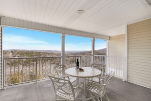 A covered balcony with a round table and chairs, overlooking a scenic landscape.