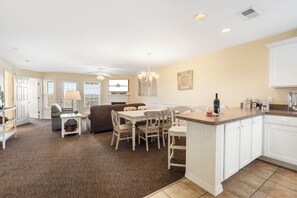 A modern kitchen with white cabinetry, a dining area with a table and chairs, and a living room with a sofa and a television. - Relaxed Lake-Access Condo with Outdoor Pool, Mini Golf, Pickleball & Free Attraction Tickets (Kimberling City)