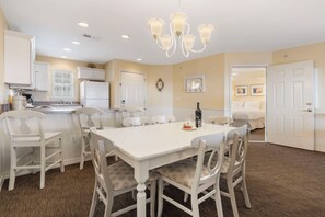 A dining area with a white table and chairs, a chandelier, and a kitchen in the background. - Relaxed Lake-Access Condo with Outdoor Pool, Mini Golf, Pickleball & Free Attraction Tickets (Kimberling City)