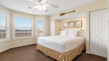 A bedroom with a large bed, a ceiling fan, and a view of the city through the windows.
