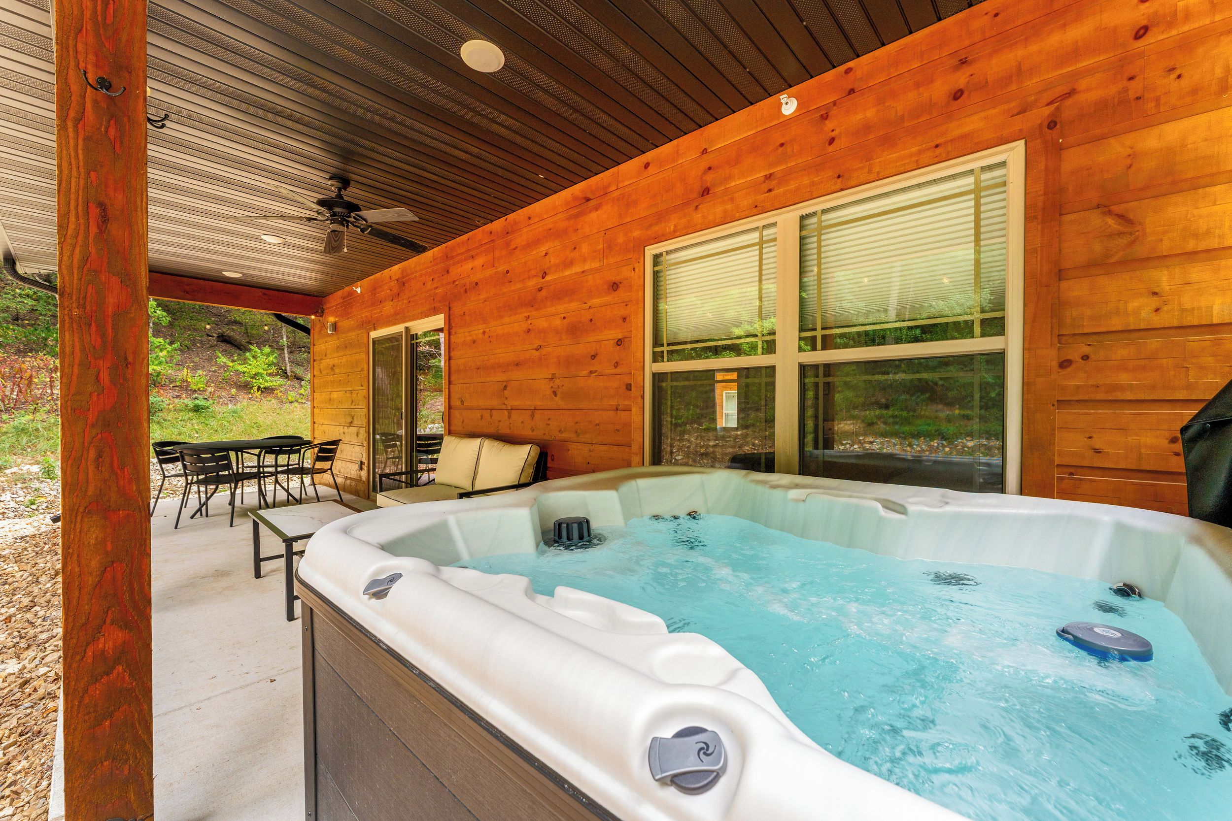 A wooden cabin with a hot tub, outdoor seating, and a covered patio.