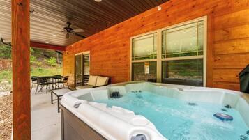 A wooden cabin with a hot tub, outdoor seating, and a covered patio.