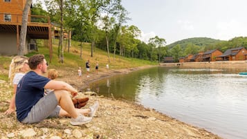 A lakeside setting with a wooden deck, a building with a covered area, and a group of people by the water.