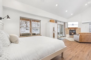 Camera da letto moderna con un ampio letto, televisione, camino e vista su un paesaggio innevato.