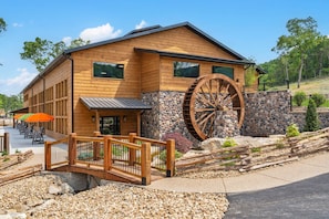 Un edificio in legno con una grande ruota idraulica, un muro in pietra e un ponte di legno.