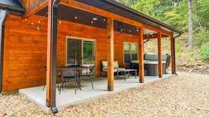 A wooden cabin with a covered patio, outdoor seating, and a grill area.