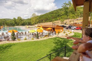 A pool area with lounge chairs and umbrellas, a wooden building, and a parking area with vehicles.